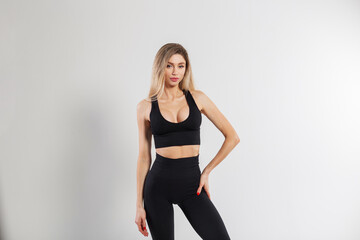 Fototapeta premium Beautiful blonde athletic fitness lady in sports fashionable black clothes with a top and leggings on a white background