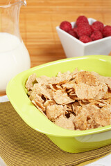 A bowl of cornflakes, milk and raspberries on bamboo mat