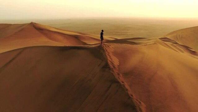 Travel, drone and thinking with man in desert for hiking, adventure and freedom. Sunset, discover and hobby with person in open space on Namibia sand dune hill for explorer, vacation and journey