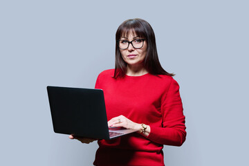 Serious mature woman using laptop looking at camera on grey background