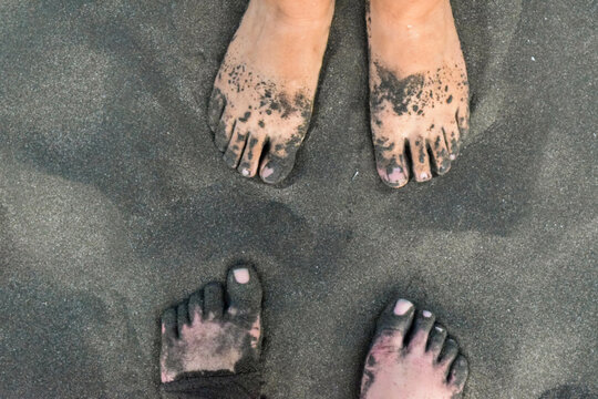 Two pairs of feet in black sand 