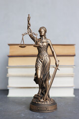 themis goddess of justice statuette on background of books on desktop. symbol of law with scales and sword in his hands. legal company or university of law and judicial structure. library education