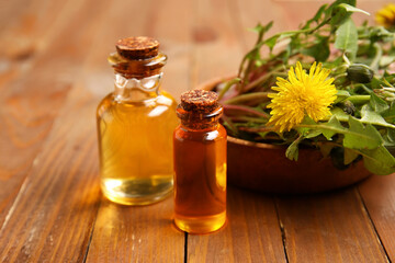 Bottles with cosmetic oil and bowl of dandelion flowers on wooden background