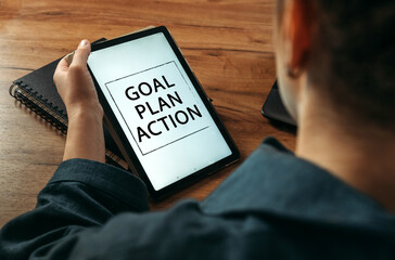 A woman holds a tablet in her hands on the screen of which it is written - goal, plan, action
