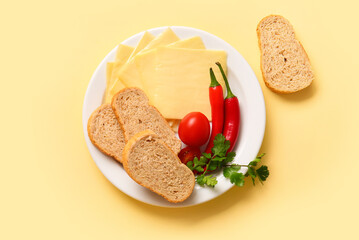 Plate of tasty processed cheese with bread and vegetables on yellow background