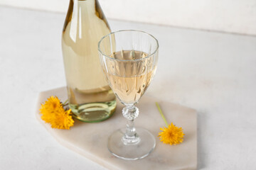Board with bottle and glass of dandelion wine on white table