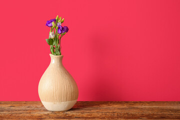 Vase with eustoma flowers on wooden table near red wall