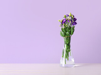 Vase with eustoma flowers on wooden table near lilac wall