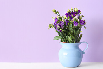 Fototapeta na wymiar Jug with eustoma flowers on table near lilac wall