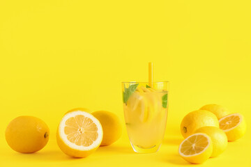 Glass with fresh lemonade and lemons on yellow background