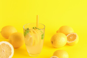 Glass with fresh lemonade and lemons on yellow background