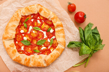 Baking paper with tasty tomato galette and basil on beige background
