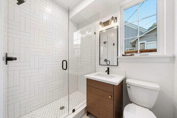 Modern bathroom with a dark brown wooden cabinet, marble countertop, and a glass shower with white subway tiles laid in a unique pattern