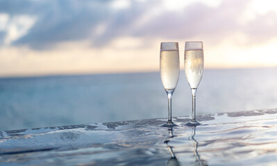 Two glasses of champagne on the side of the infinity pool against the backdrop of a sunset in the...