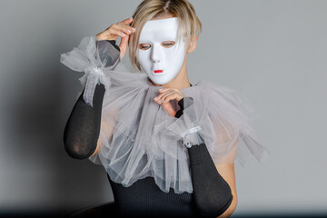 Face behind mask. Woman in white theater mask and harlequin collar on gray background. Fancy dress, masquerade clothes 