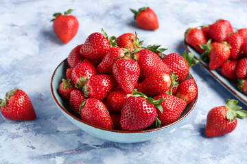 Bowl and plate with fresh strawberries on blue background