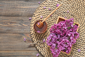 Wicker mat and box of beautiful lilac flowers with honey on brown wooden background