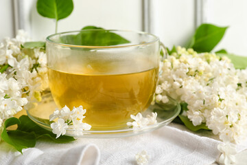Cup of tea and lilac flowers near white wooden wall