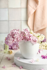Obraz na płótnie Canvas Cup of beautiful fragrant lilac flowers on stand near white tile