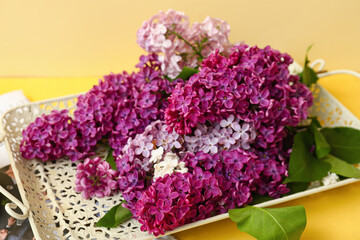 Tray with beautiful fragrant lilac flowers and magazine on pale yellow background