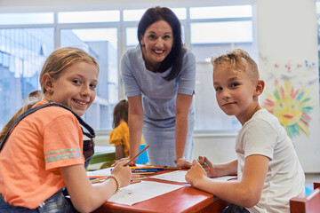 Creative kids during an art class in a daycare center or elementary school classroom drawing with female teacher.