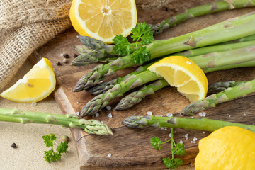 Fresh green asparagus bunch with lemon slices and parsley leaves on wooden board.