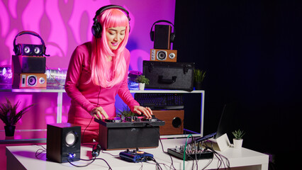 Smiling musician working as dj playing song at mixer console, mixing techno music with eletronic using audio equipment. Performer with pink hair having fun in performing in club at night time