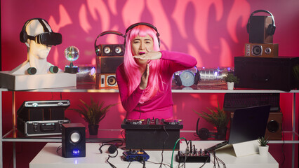 Asian artist with pink hair performing techno music using dj mixer console enjoying to play song with fans, having fun in club at night. Musician doing performance with professional audio equipment