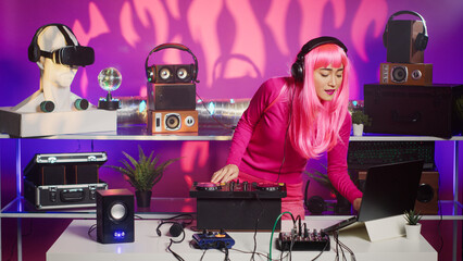 Musician with pink hair performing techno music using dj mixer console enjoying to play song with fans, having fun during night party. Artist doing performance with professional audio equipment
