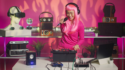 Musician talking with fans into microphone during party, performing techno remix using professional turntables. Asian performer mixing sounds while dancing and having fun in nightclub