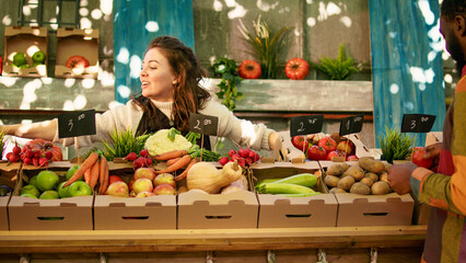 People enjoying shopping at local farmers market, checking fresh farm produce. Young diverse couple...