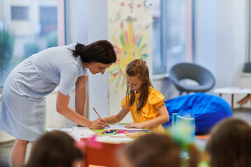 Creative kids during an art class in a daycare center or elementary school classroom drawing with female teacher.