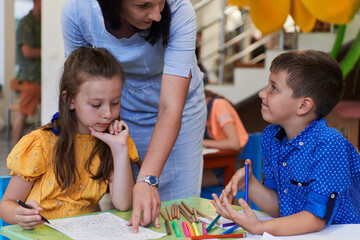 Obraz premium Creative kids during an art class in a daycare center or elementary school classroom drawing with female teacher.