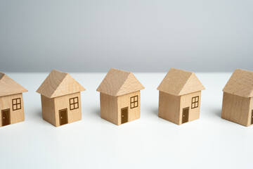 Wooden toy houses stand in a row. Find most suitable housing options. Offers on real estate market. Mortgage. Valuation of residential buildings. Realtor services. Buying and selling.