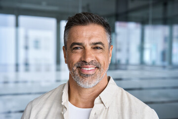 Headshot close up portrait of indian or latin confident mature good looking middle age leader, ceo male businessman on blur office background. Handsome hispanic senior business man smiling at camera.