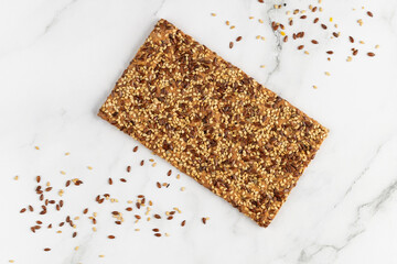 Crispy whole cereal bread with flax and sesame seeds on white marble background.