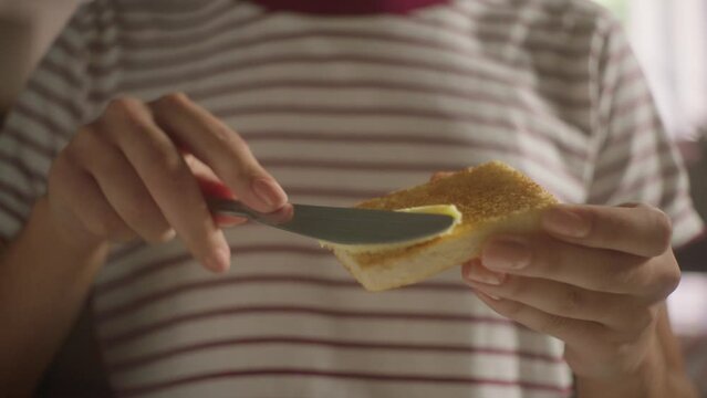 super close-up of hand buttering bread in slow motion and zoom out, background striped shirt 