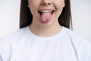 Cropped view. Face of a teenage girl in white t-shirt, showing tongue isolated on white background