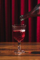 Lambrusco bottle pouring into glass, background of red velvet curtains and wooden table
