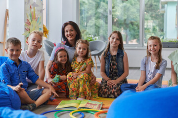 A happy female teacher sitting and playing hand games with a group of little schoolchildren