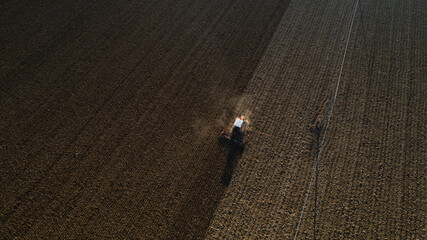 farmer driving a crawler tractor drags a cloud of dust behind, ploughing, power harrowing surface...