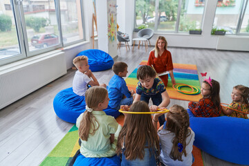 A happy female teacher sitting and playing hand games with a group of little schoolchildren