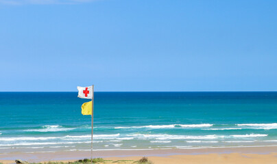 beach on yellow flag alert for the sea and the red cross flag of the first aid post
