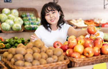 Pleased young woman customer taking ripe apples at the counter in large greengrocery
