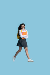 Full-length studio portrait of happy teenage student girl carrying backpack over yellow background