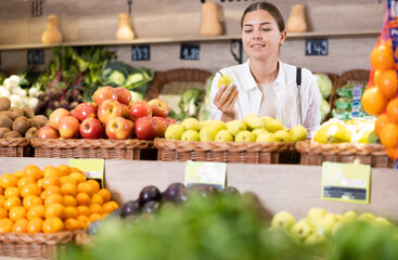 Delighted young woman purchaser choosing pears at the counter in large grocery store