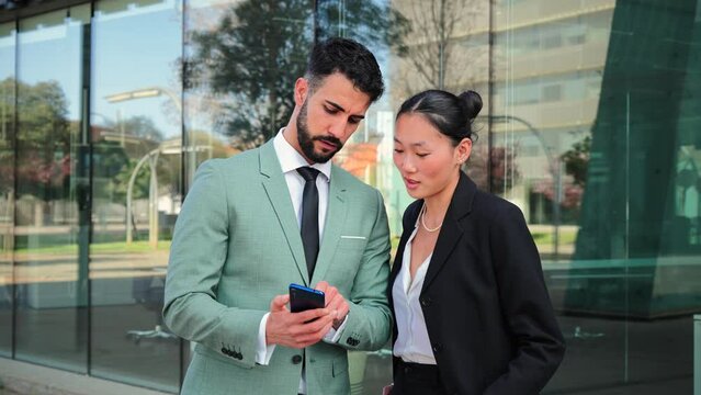 A couple of executive business people colleagues or lawyers using a cellphone to plan the job. Successful start up teamwork talking about the stock selling strategy watching a smartphone at workspace