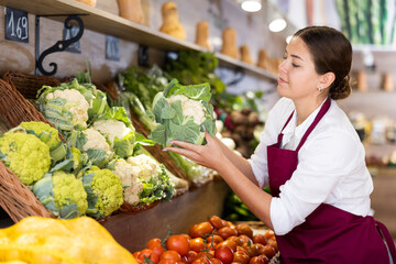 Young saleswoman puts fresh cauliflower on the supermarket shelves