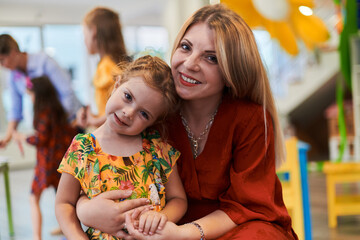 A cute little girl kissing and hugs her mother in preschool