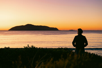 Fototapeta na wymiar Silhouette of man standing on sand dune overlooking Jimmy's Beach at sunrise. Hawks Nest, NSW Australia